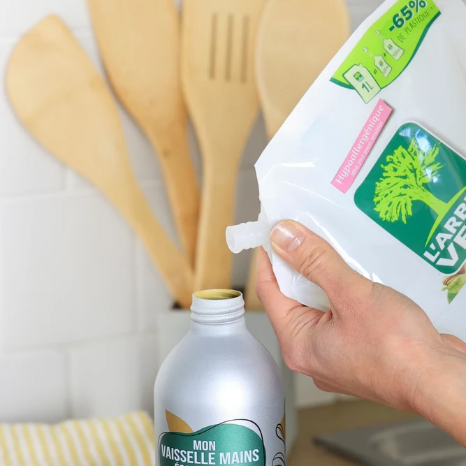 Une main versant le contenu d'une éco-recharge de liquide vaisselle L'Arbre Vert dans un flacon réutilisable en aluminium.