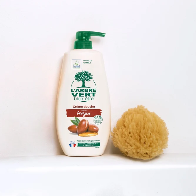 Grand flacon pompe de crème douche L'Arbre Vert bien-être au parfum Argan de 720 ml, posé à côté d'une éponge de mer naturelle.