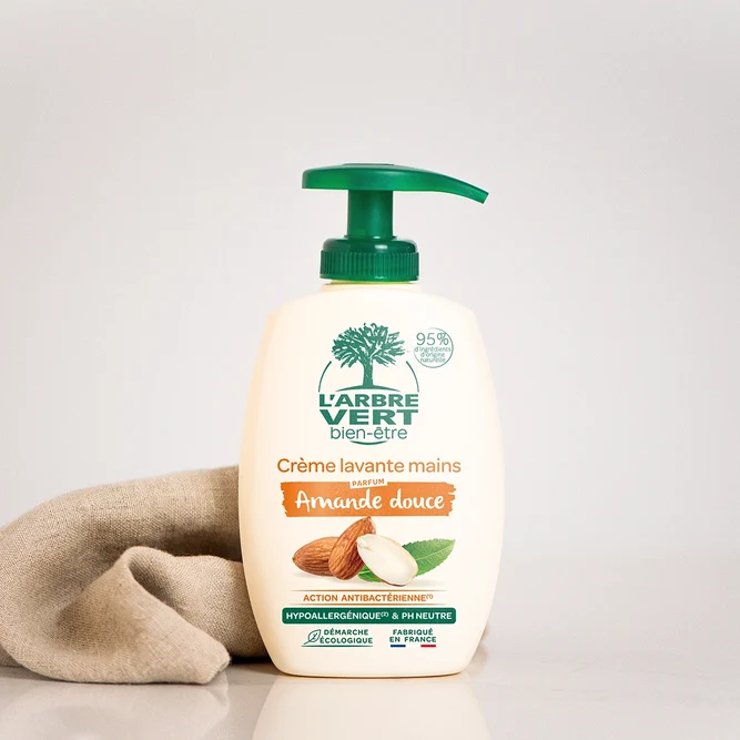 Flacon pompe de 300 ml de Crème lavante mains L'Arbre Vert bien-être au parfum Amande douce, posé à côté d'un tissu naturel.