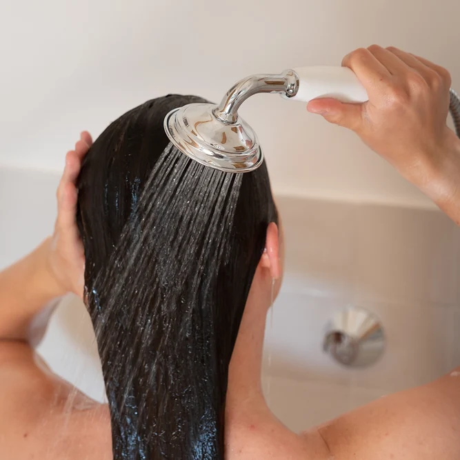 Een persoon die haar bruin haar spoelt onder de straal van de douche.
