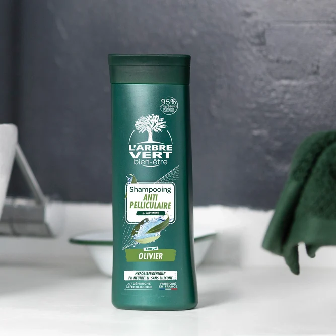 Flacon vert de 250 ml de shampooing Antipelliculaire L'Arbre Vert bien-être à la saponine et au parfum Olivier, posé au bord d'un lavabo.